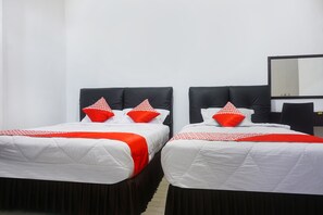Two single beds with black headboards, white bedding, and red pillows.
