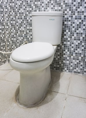 A toilet with a white tank and seat, set against a tiled wall with a checkered pattern.