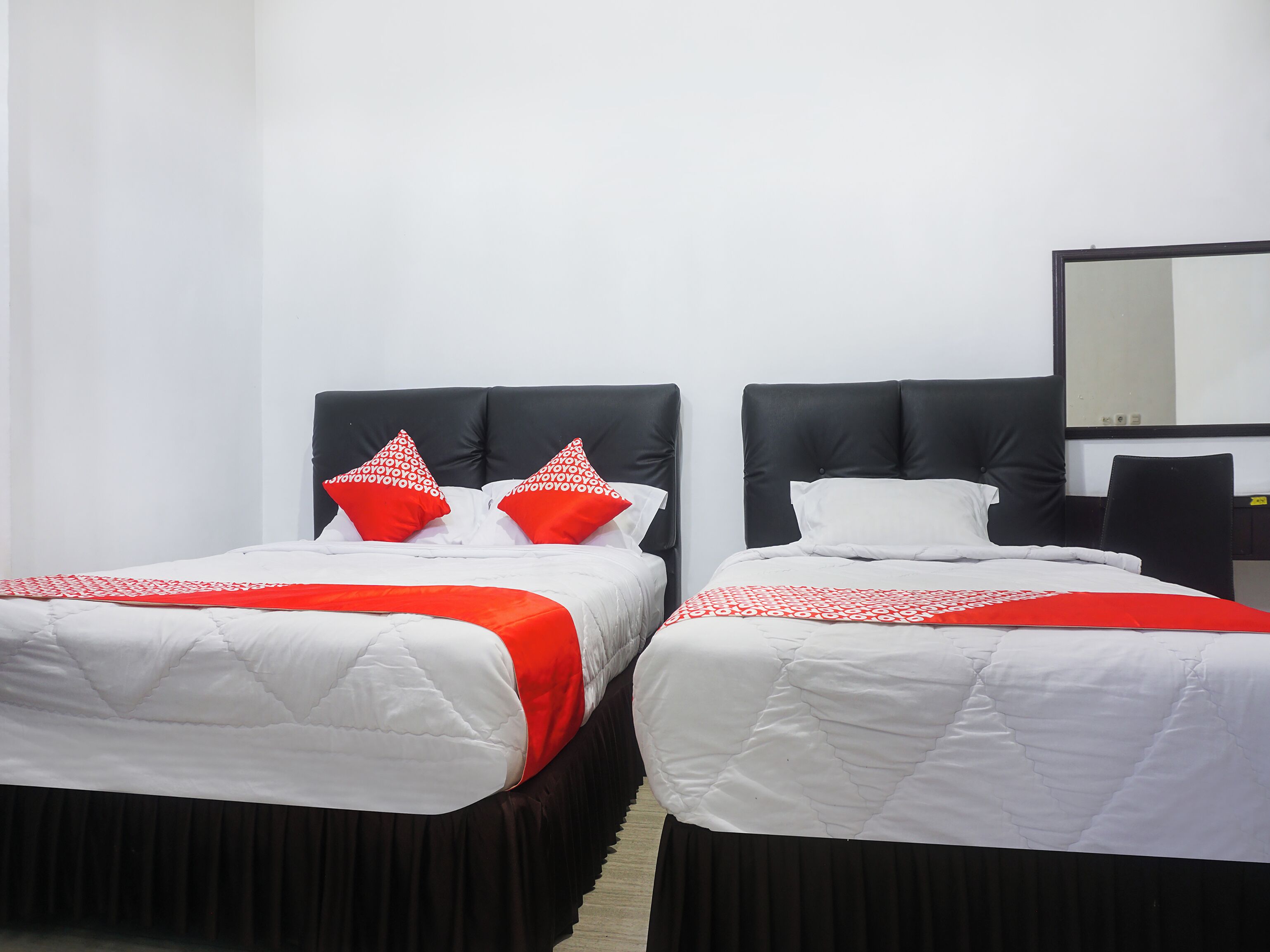Two single beds with black headboards and white bedding, a black chair, and a mirror on the wall.