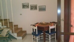 A dining area with a wooden table and white chairs, a wicker chair, and a staircase. - Cottage by the sea of salento (Santa Cateria di Nardo)