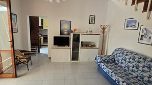 A living room with a sofa, a television, and a kitchen in the background. - Cottage by the sea of salento (Santa Cateria di Nardo)