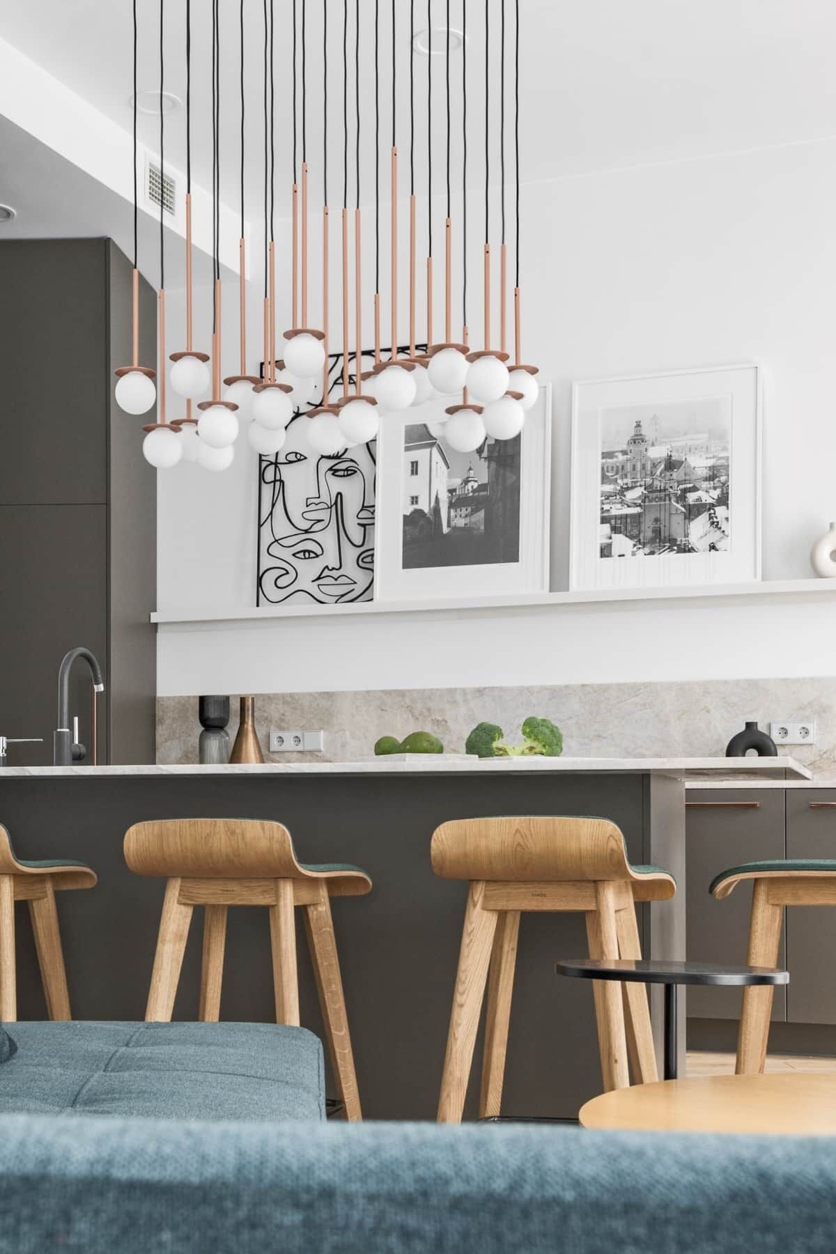 A modern kitchen with a central island, pendant lights, and wooden chairs.