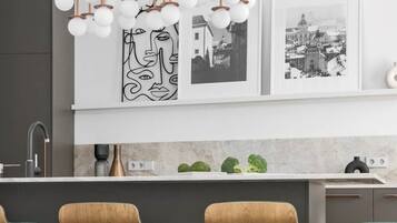 A modern kitchen with a central island, pendant lights, and wooden chairs.
