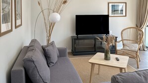 Una sala de estar moderna con un sofá gris, una mesa de centro, una silla de mimbre y un televisor de pantalla plana.