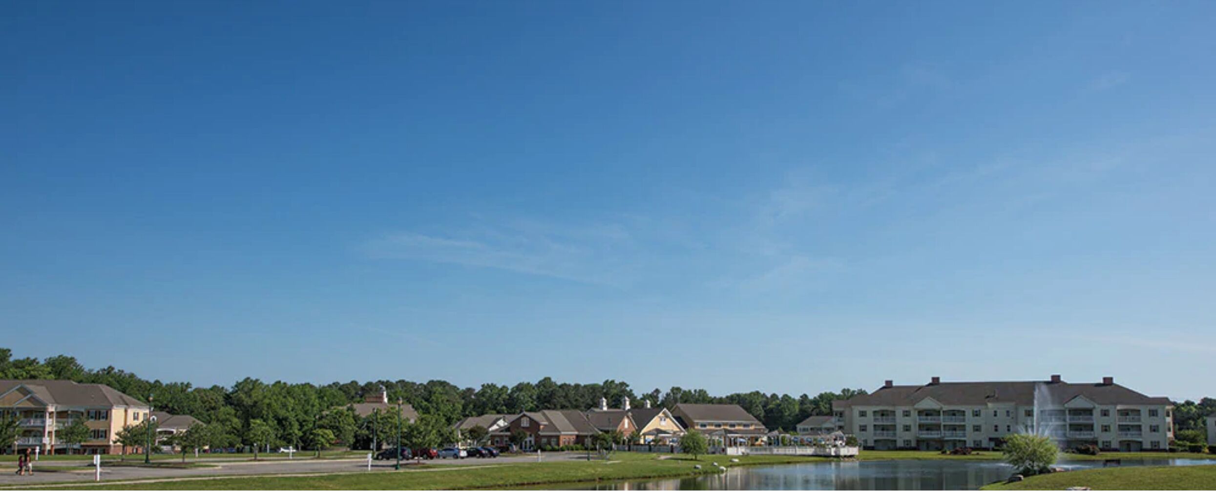 A lakeside view of a hotel with multiple buildings, a fountain, and a clear blue sky.