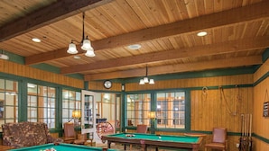 Een poolzaal met houten wanden, groene accenten en meerdere pooltafels.