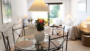 A modern living room with a glass dining table, white sofas, and a large window with natural light. - Los Piños, 2 Bedroom Apartment with panoramic view (Benahavis)