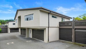 A modern two-story residential building with a garage, a driveway, and a clear blue sky. - Adventure Trails - Spa Pool, Walk to Redwoods (Rotorua)