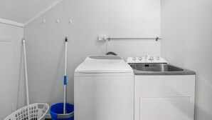 A laundry room with a washing machine, a sink, a mop, and a laundry basket. - Adventure Trails - Spa Pool, Walk to Redwoods (Rotorua)