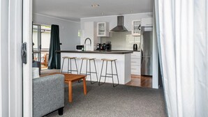 A modern kitchen with a central island, bar stools, and a dining area with a table and chairs. - Adventure Trails - Spa Pool, Walk to Redwoods (Rotorua)