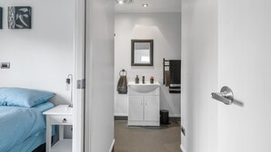 A hotel room with a bed, a bedside table, a white cabinet, a mirror, and a door. - Adventure Trails - Spa Pool, Walk to Redwoods (Rotorua)