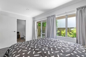 A bedroom with a large bed, a sliding glass door leading to a balcony, and a view of greenery outside. - Adventure Trails - Spa Pool, Walk to Redwoods (Rotorua)