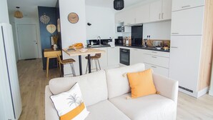 A modern kitchen with white cabinets, a black countertop, and a dining area with a wooden table and bar stools. - -SHELBY- T2 ARRIÈRE CORNICHE PARKING ET TERRASSE (Concarneau)