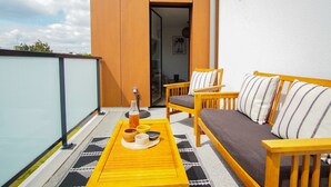 A balcony with a yellow table, wooden chairs, and a sofa. - -SHELBY- T2 ARRIÈRE CORNICHE PARKING ET TERRASSE (Concarneau)