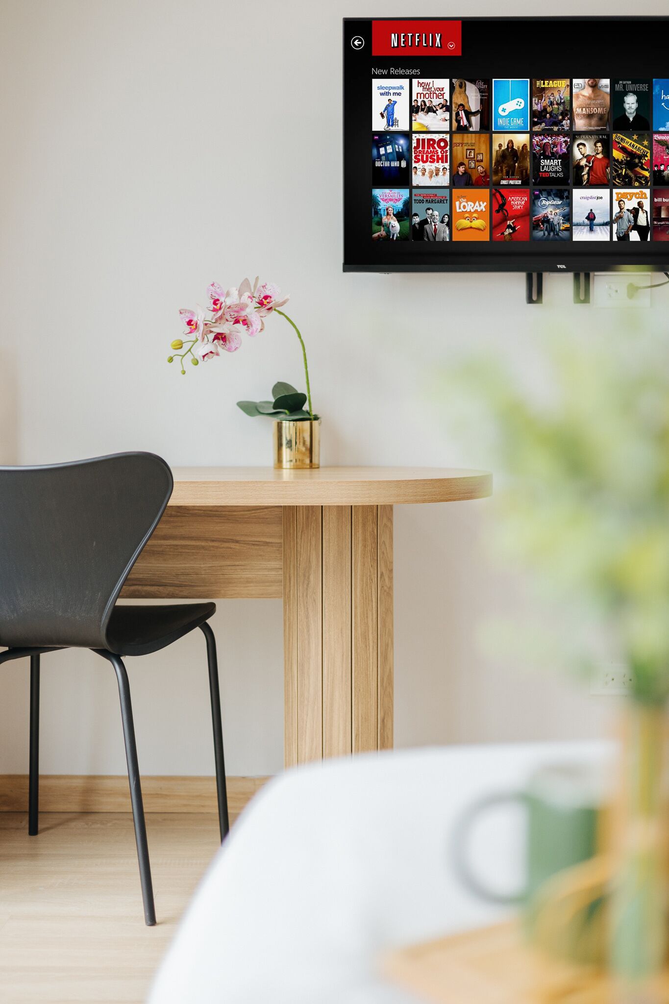 A modern room with a wooden table, a black chair, and a wall-mounted TV displaying a Netflix interface.