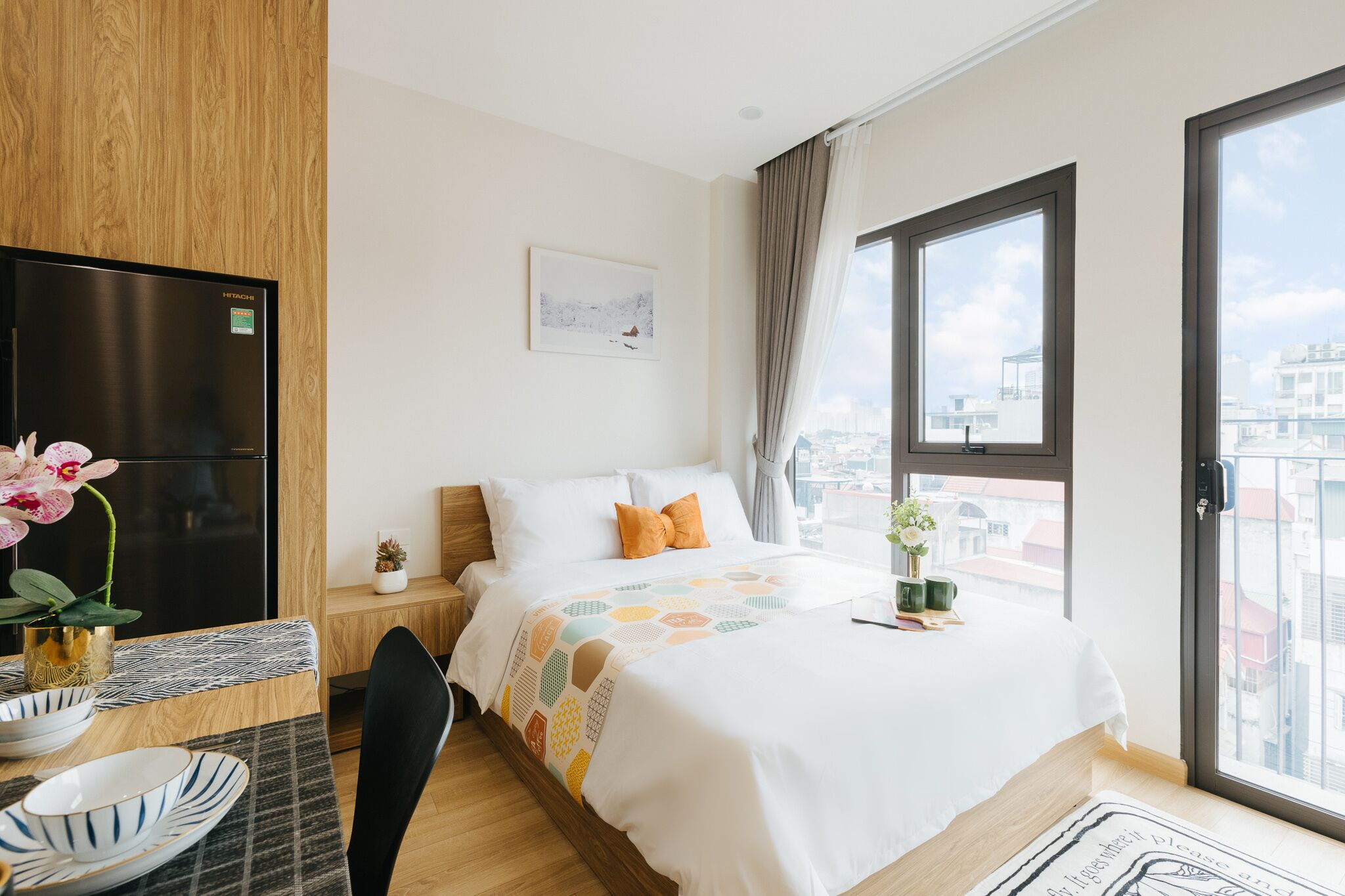 Una habitación de hotel moderna con cama, zona de comedor, televisión y un ventanal con vistas a la ciudad.
