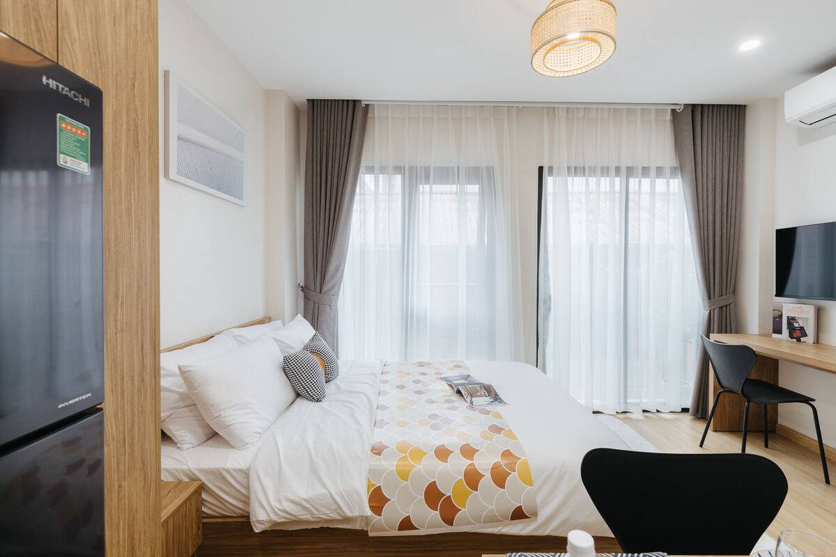Quarto de hotel com cama, escrivaninha com cadeira, televisão e frigorífico.