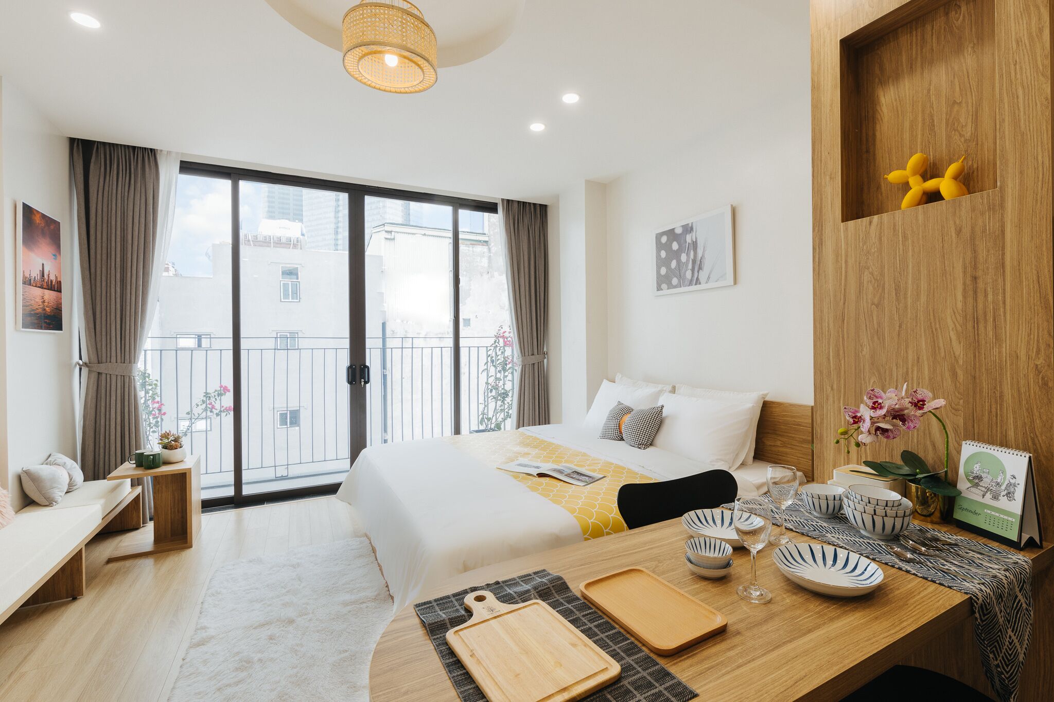 Een hotelkamer met een groot bed, een houten bureau met servies, een kleine tafel en een balkon met uitzicht op gebouwen.