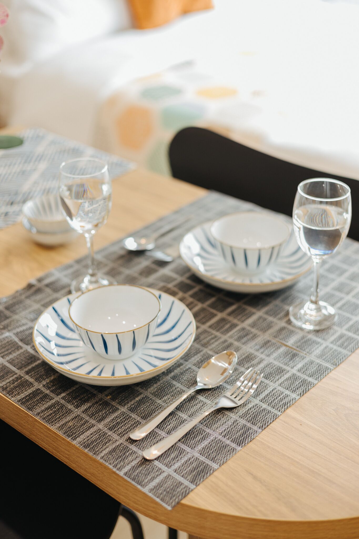A neatly set dining table with a placemat, plates, cutlery, and glasses.