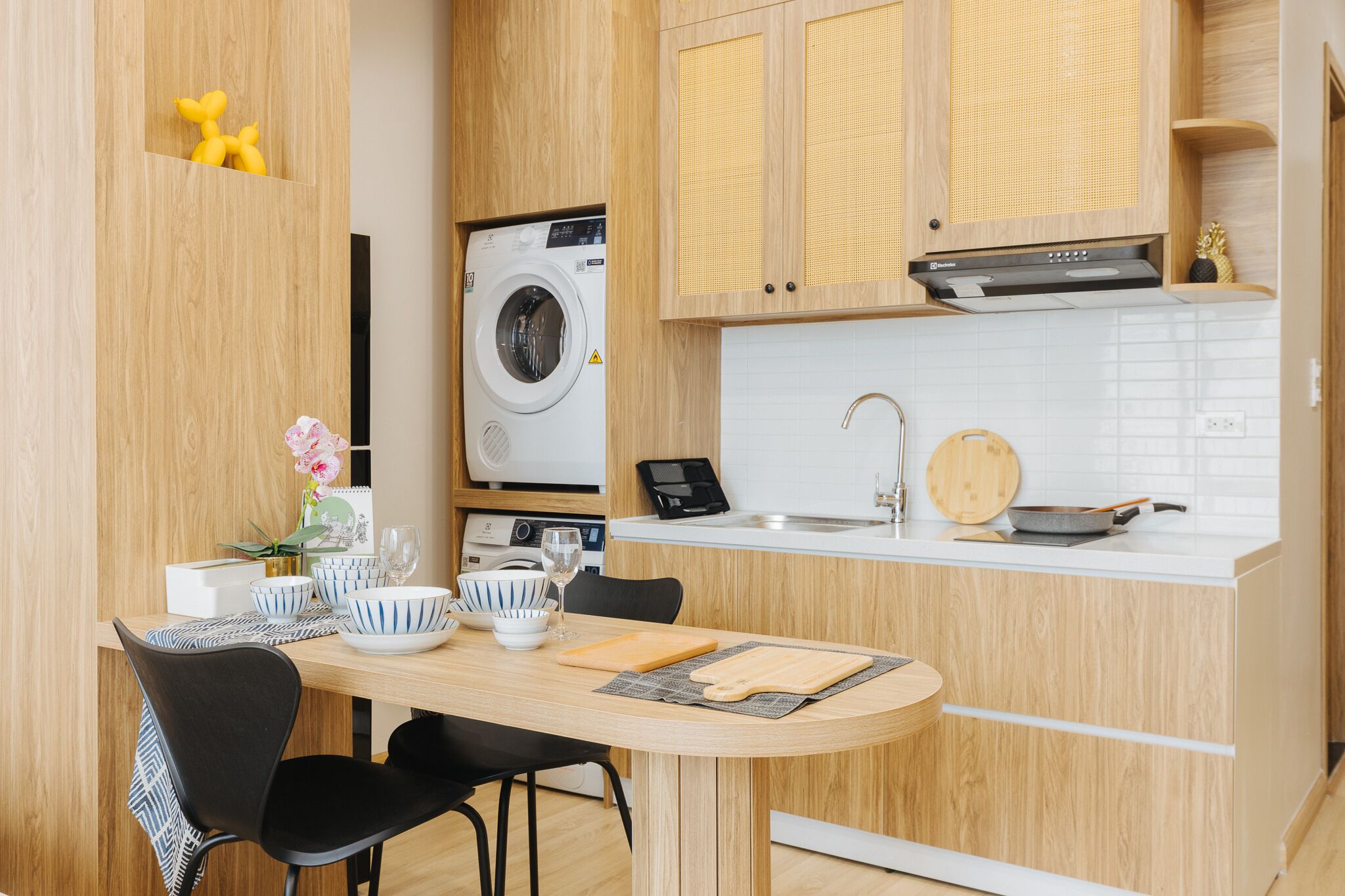 Una cocina compacta con lavadora integrada, un comedor con mesa y sillas, y una pequeña encimera con un fregadero y una sartén.