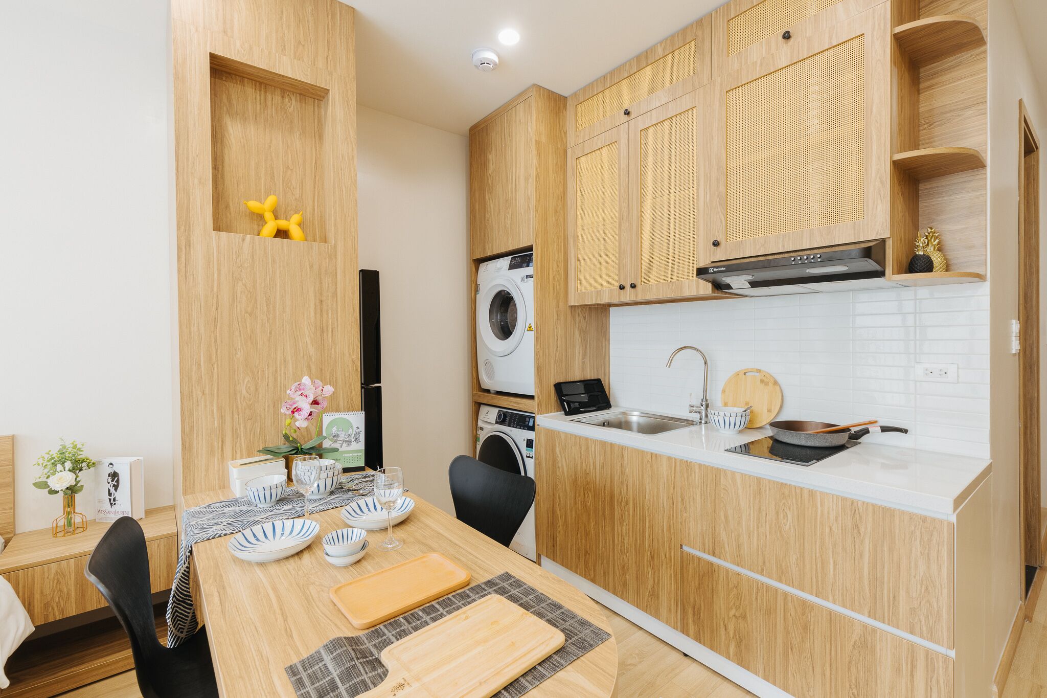 Een compacte keuken met houten kastjes, een ingebouwde wasmachine en een eethoek met een tafel gedekt voor twee personen.