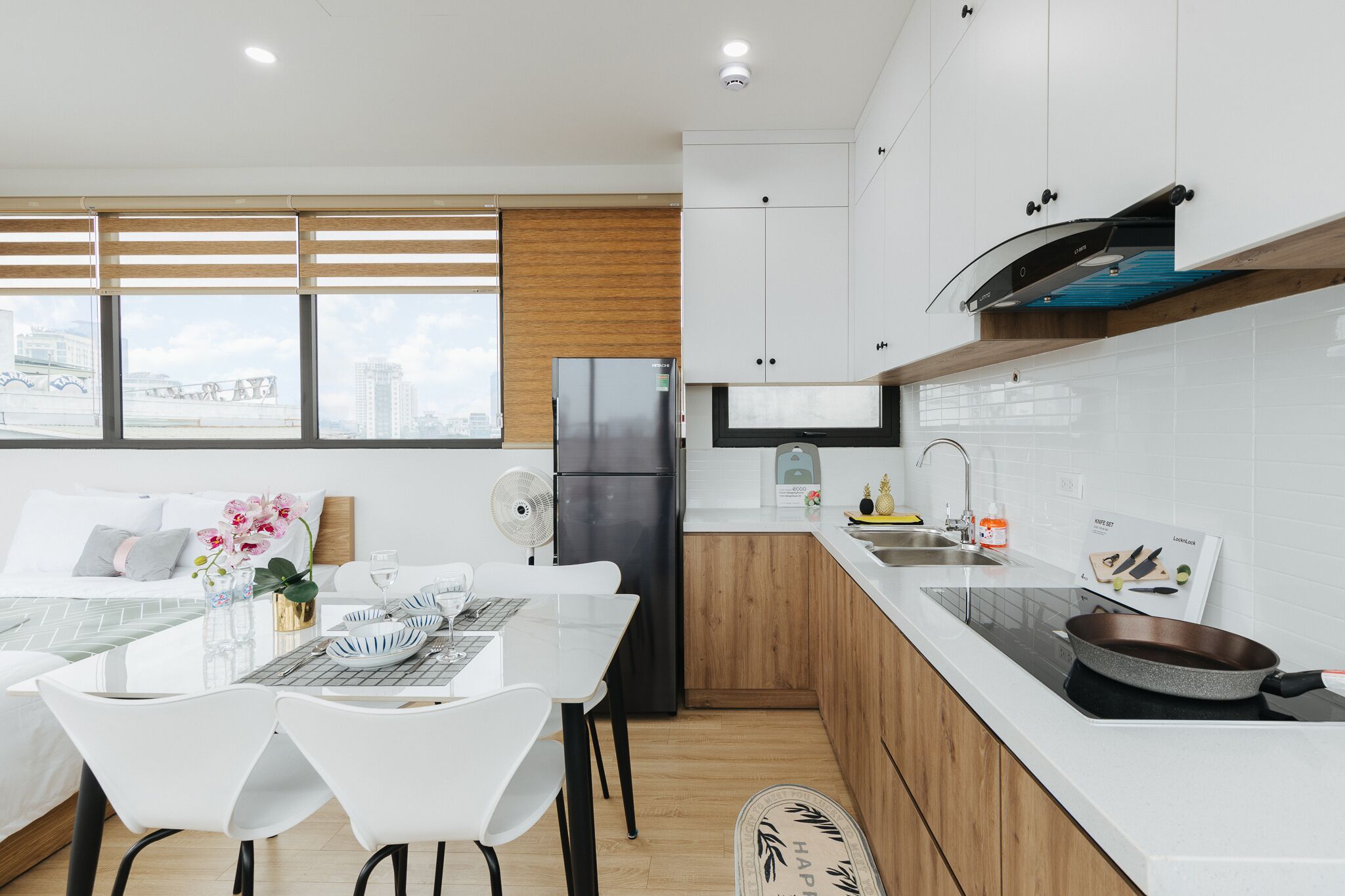 Une cuisine moderne avec des meubles blancs, un réfrigérateur noir et un coin repas comprenant des chaises et une table, le tout dans des tons blancs.