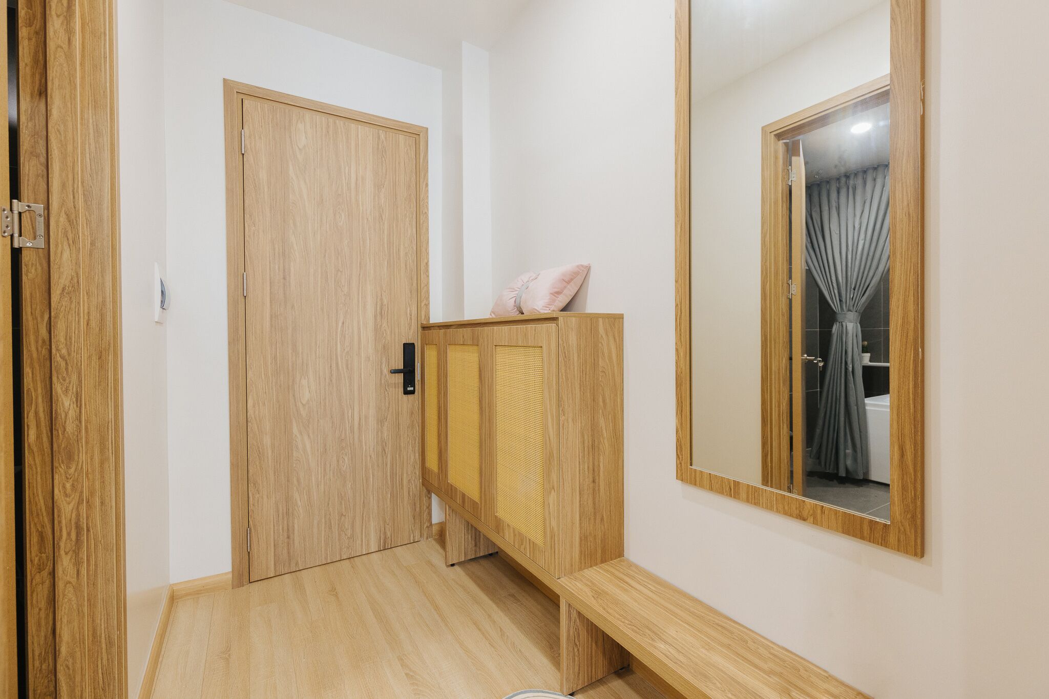 Ein Korridor mit einer Holztür, einer Bank und einem Spiegel, der ein Badezimmer widerspiegelt.