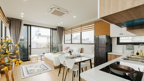 A modern kitchen with a built-in stove, a dining area with a table and chairs, and a large window with blinds. - Myrcella Urban Studio (Hanoi)