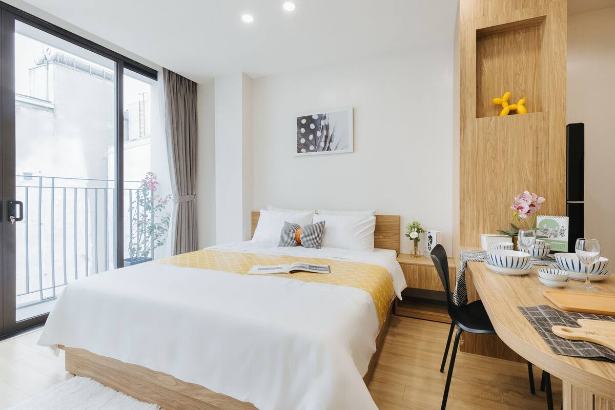 Quarto de hotel moderno com uma cama grande, área de refeições com mesa de madeira e vista para a varanda externa.