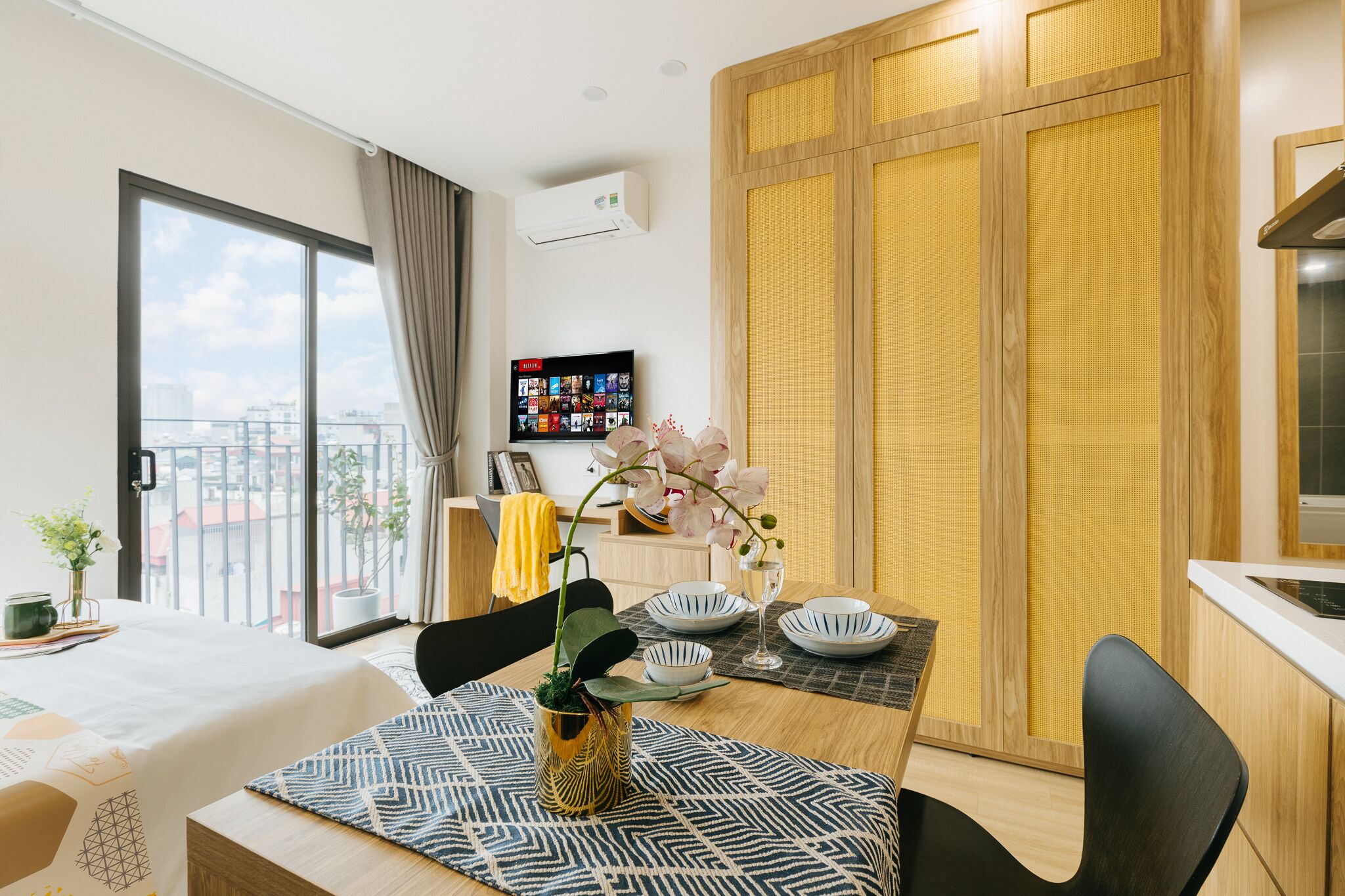 Habitación de hotel moderna con comedor, un amplio ventanal con vistas a la ciudad, zona de cocina y armario con puerta corredera.