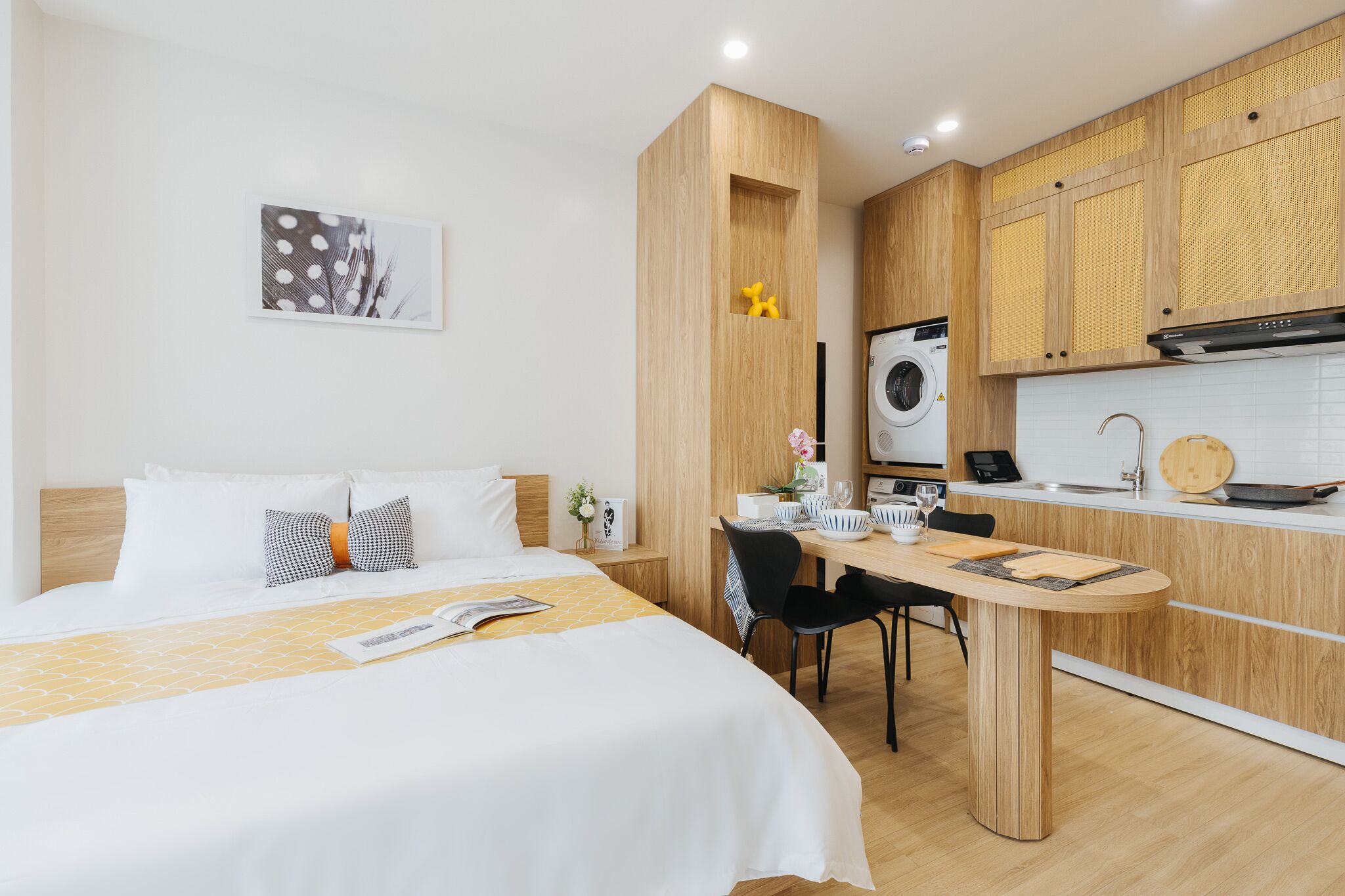 A modern hotel room with a bed, a desk, and a kitchenette.