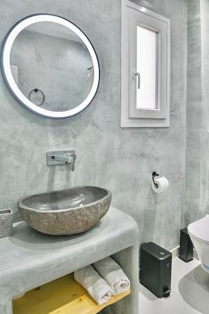 Un baño con lavamanos de piedra, un espejo redondo, un inodoro y un perchero para toallas.