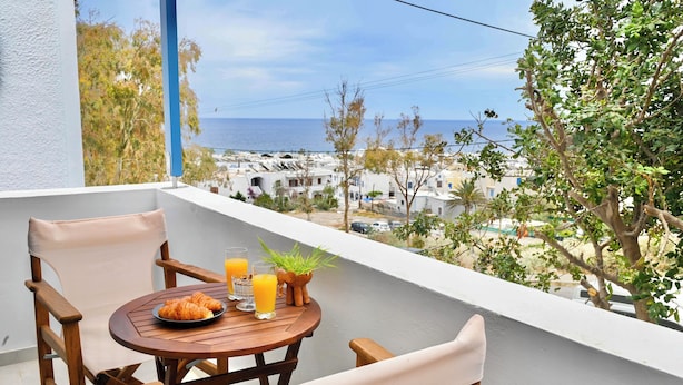 Un balcón con una mesa de madera dispuesta para el desayuno, con vista a un pueblo costero y al mar.