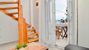 Un interior moderno con una escalera de madera, un ventanal corredero que da a una zona de estar exterior y una mesita con plantas.