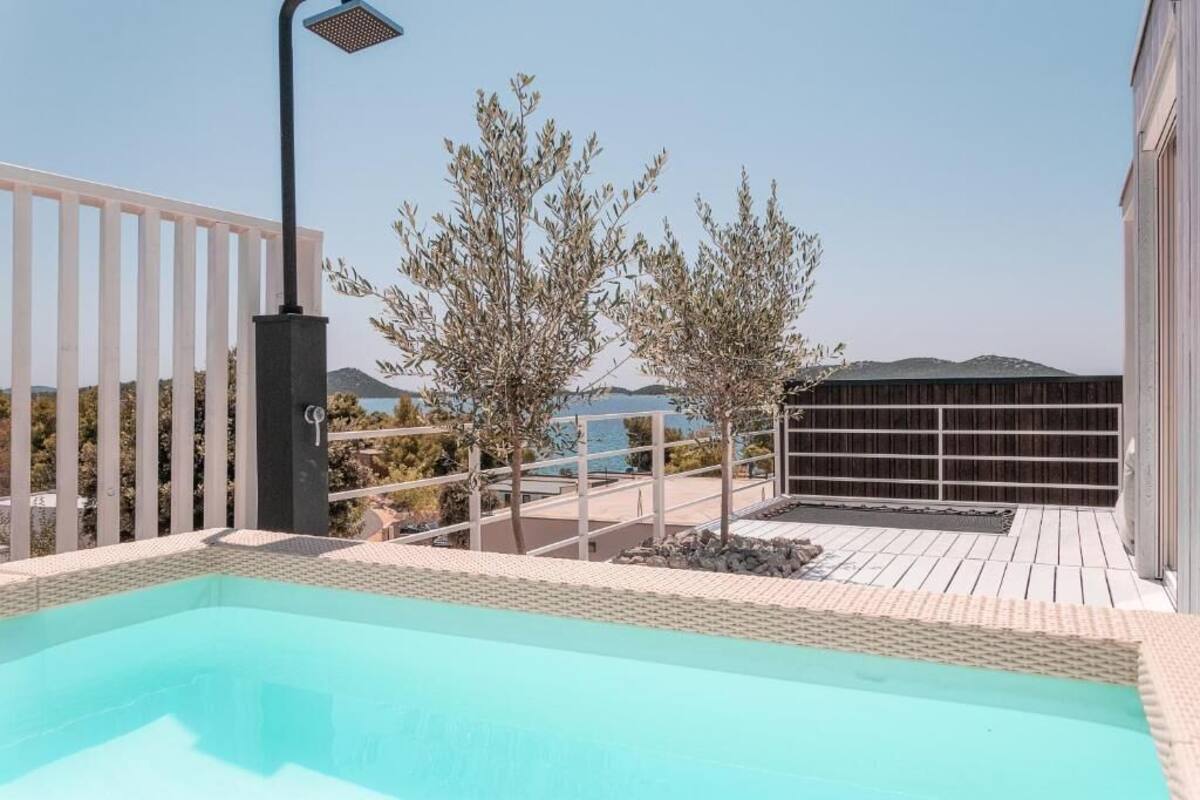 A rooftop pool area with a clear view of the sea, a pergola, and a wooden deck.