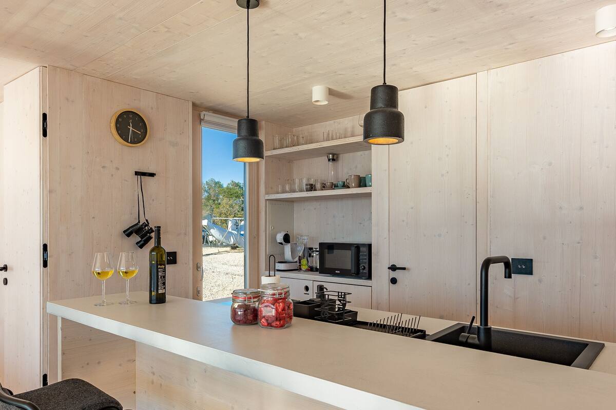 A modern kitchen with wooden cabinets, a white countertop, and hanging pendant lights.