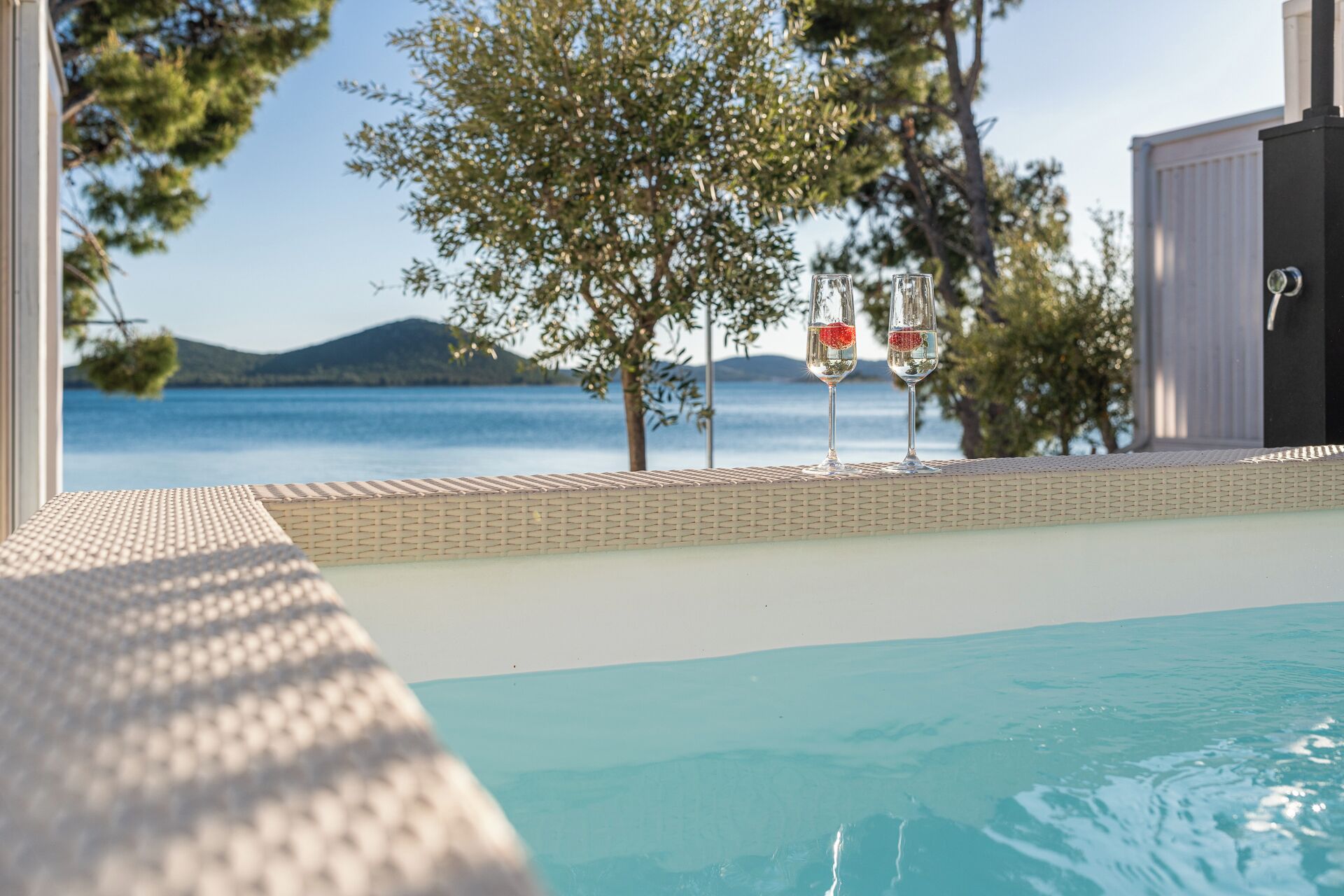 An outdoor pool area with a view of a calm sea and distant hills.