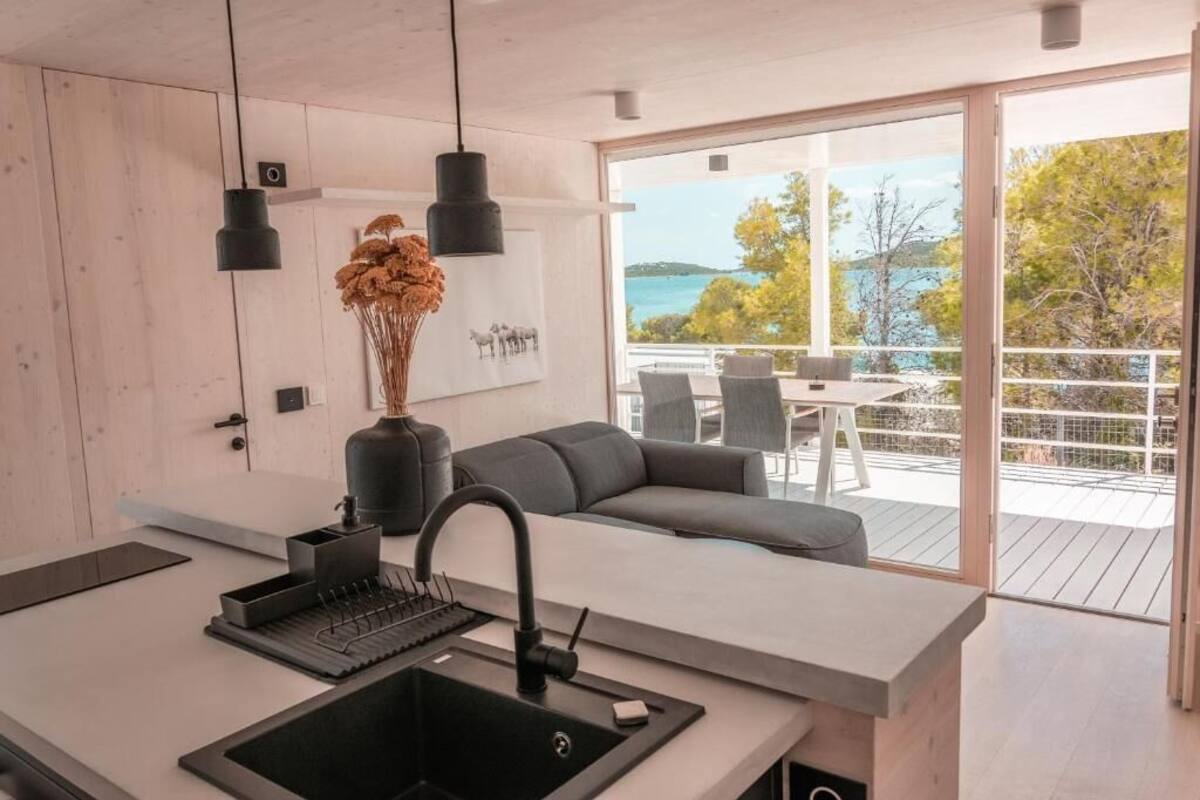A modern kitchen with a large island, black pendant lights, and a view of the outdoors.