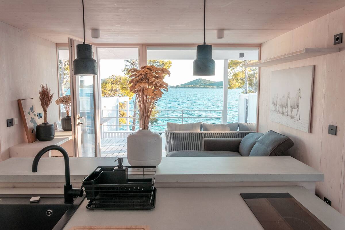 A modern kitchen with a large window overlooking a body of water, a white countertop, and a hanging pendant light.