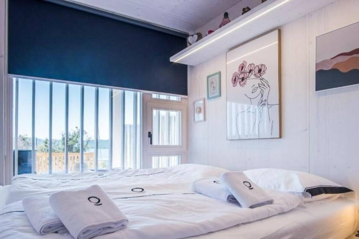 A bedroom with a large window, white bedding, and artwork on the walls.