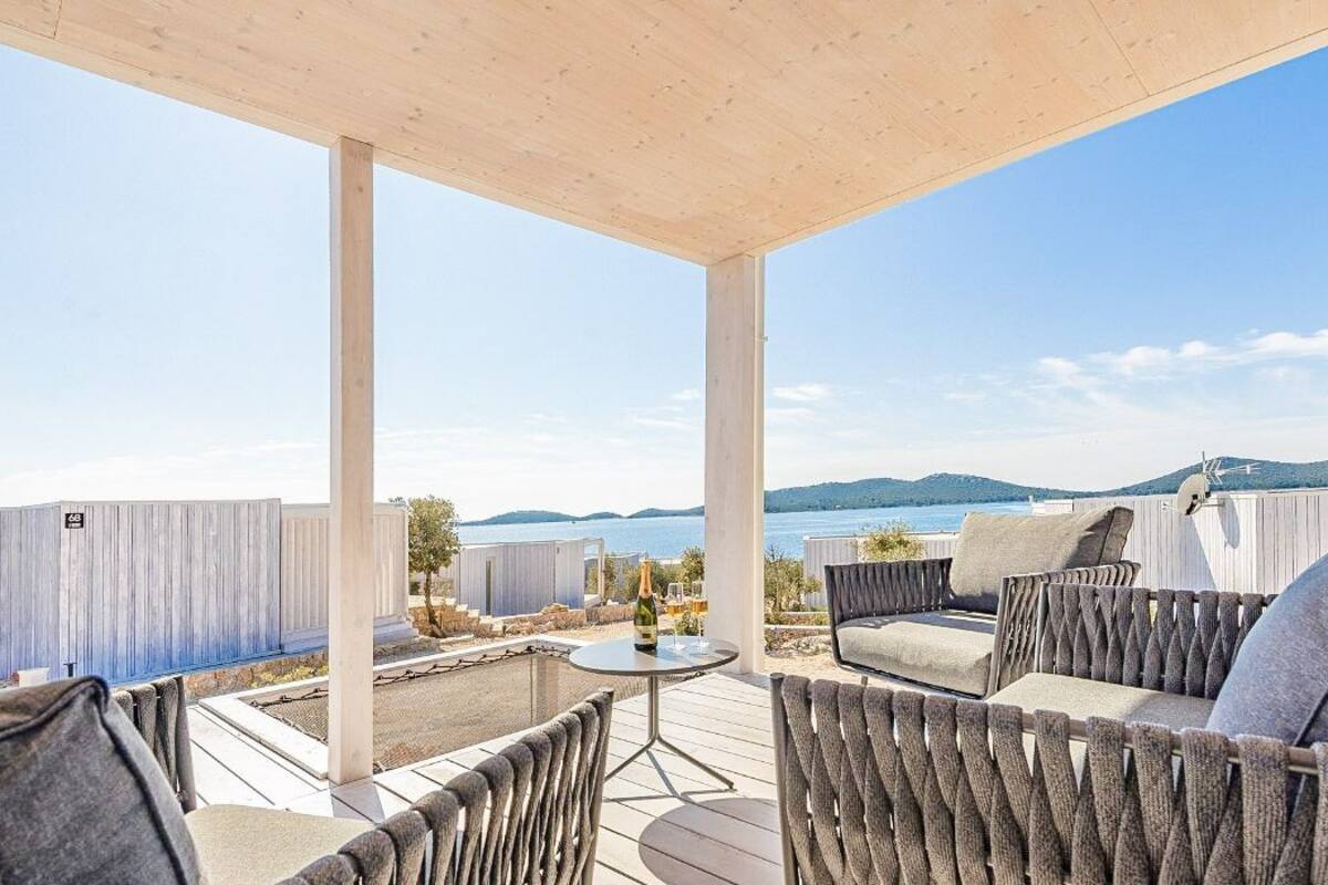 A covered outdoor seating area with a view of the sea and hills.