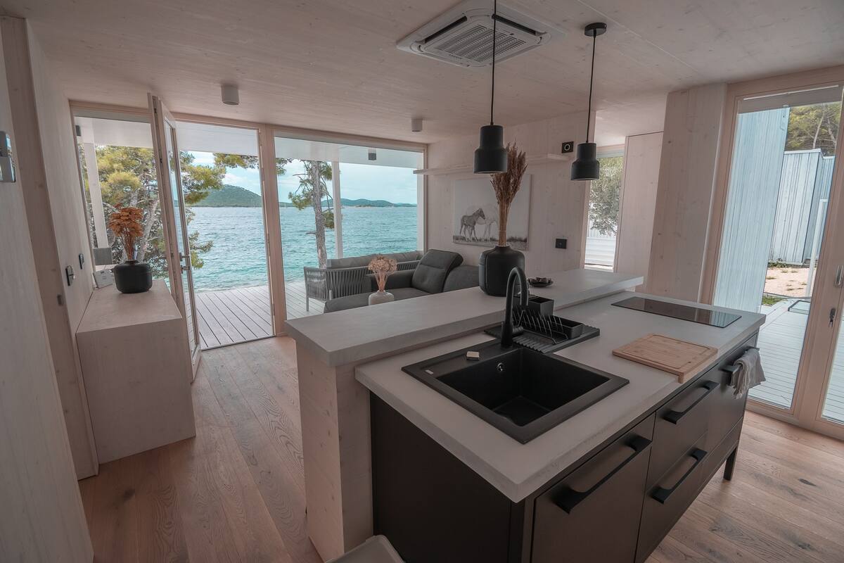 A modern kitchen with a large island, black sink, and a view of the sea.
