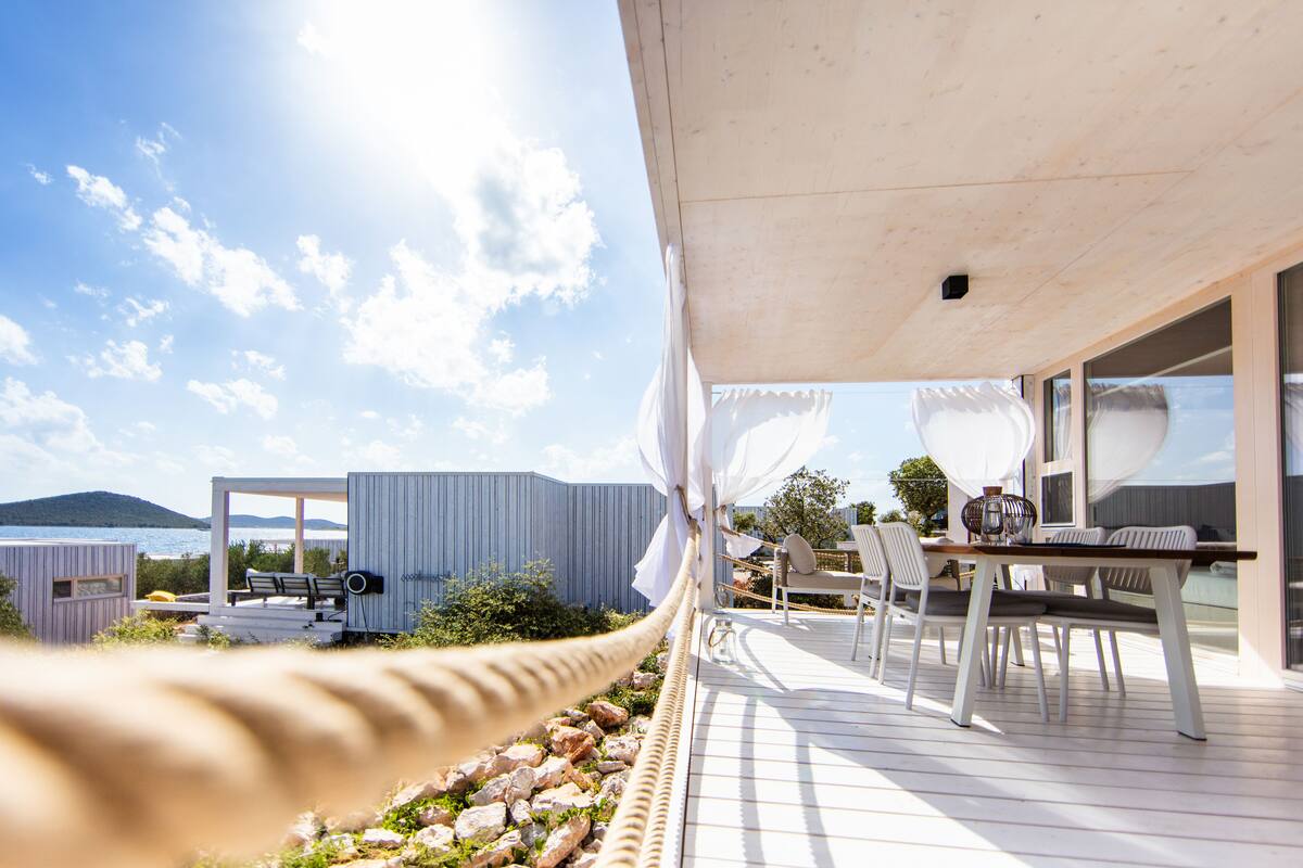 A modern outdoor deck with a wooden table and chairs, overlooking a body of water and mountains.