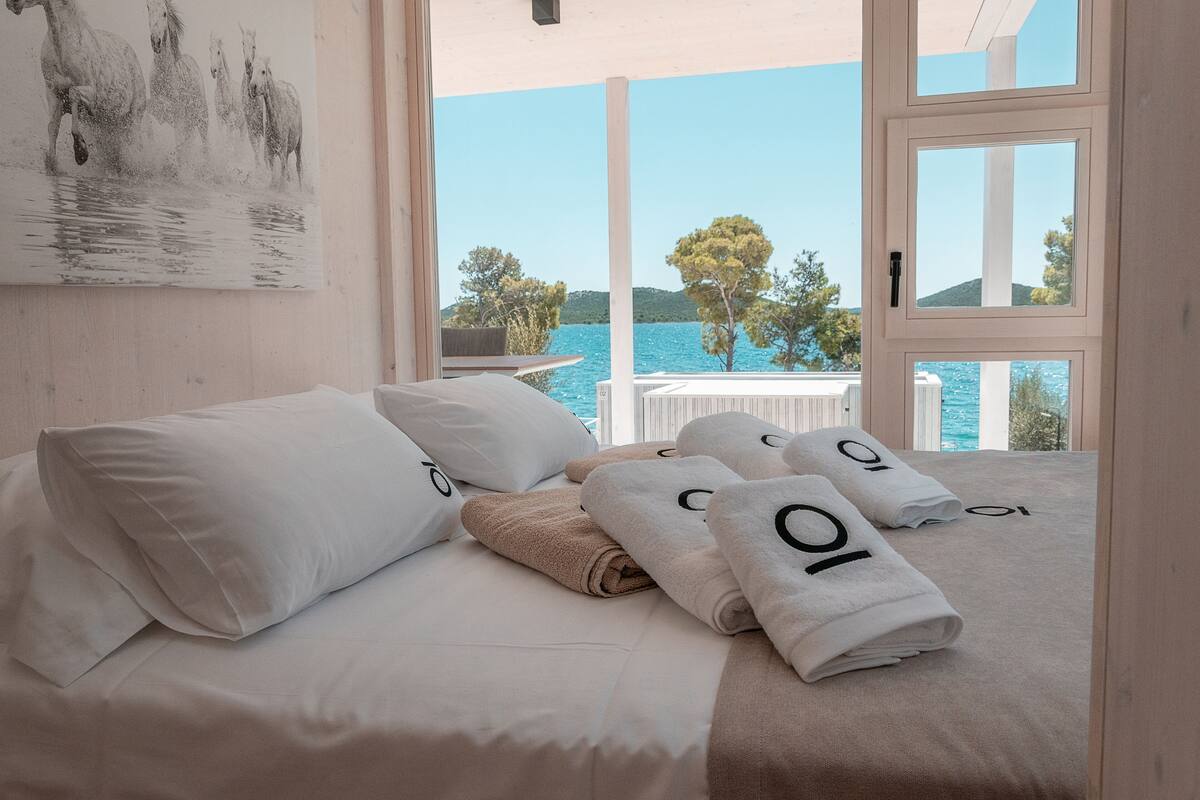 A hotel room with a bed, pillows, towels, and a view of the sea.