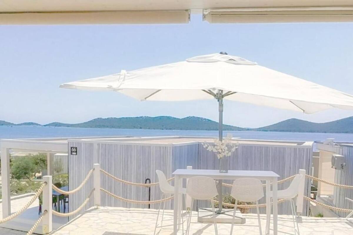 An outdoor seating area with a table and chairs under a white umbrella, overlooking a body of water and distant hills.