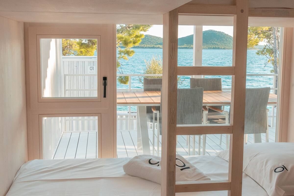 A room with two beds, a wooden door, and a view of a lake and mountains.