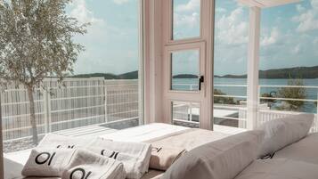 A bedroom with a large window overlooking a body of water and hills. There are two beds with white linens and towels.