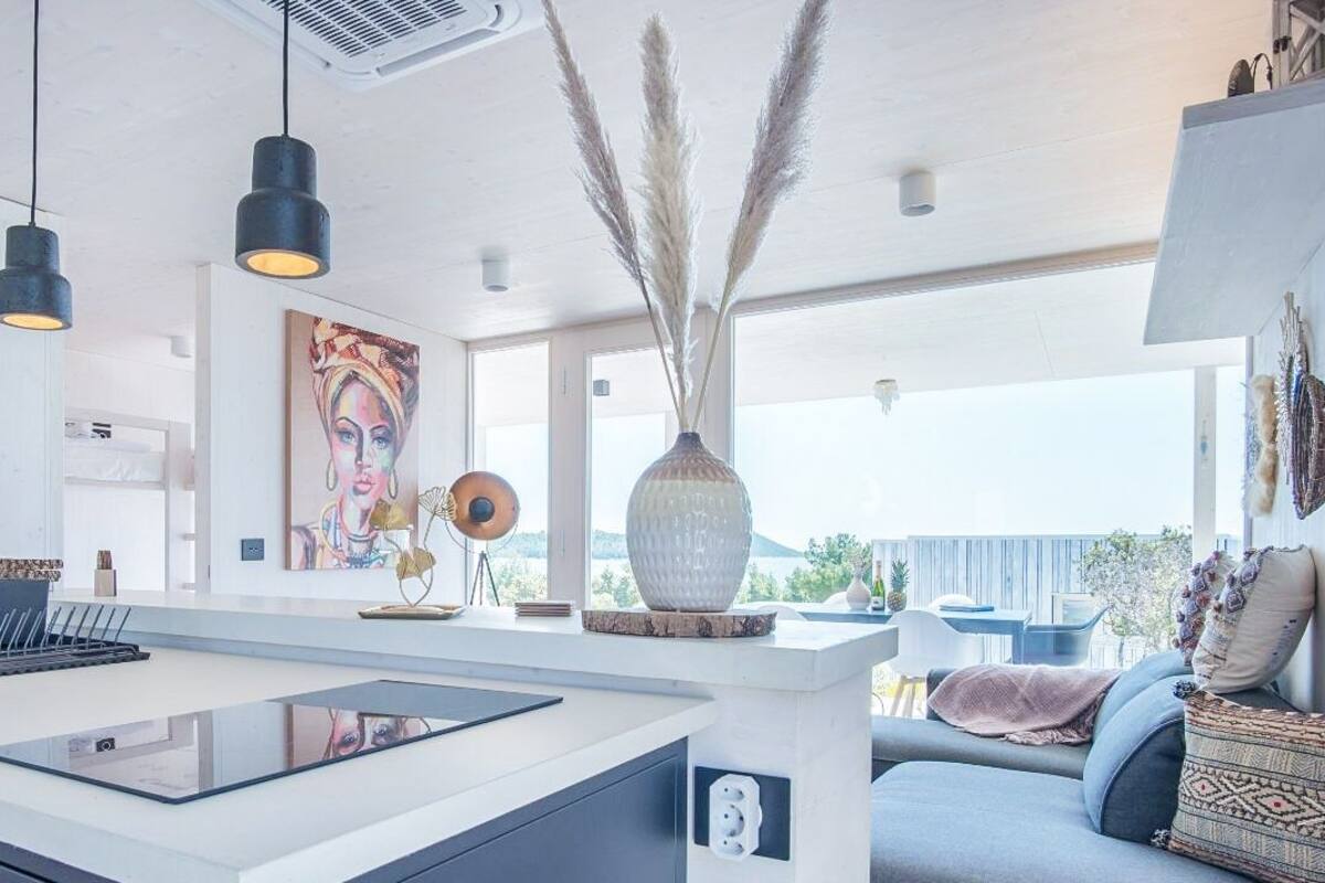 A modern kitchen with a central island, pendant lighting, and a large window offering a view.