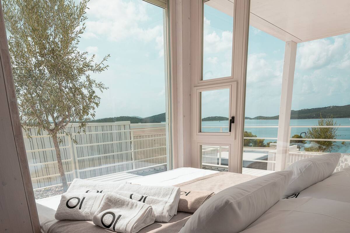 A bedroom with a large window offering a view of the sea and hills.