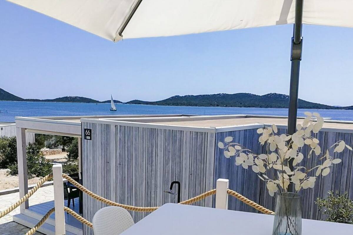 A seaside view with a table and chairs under a canopy, a wooden fence, and a number '66' sign.